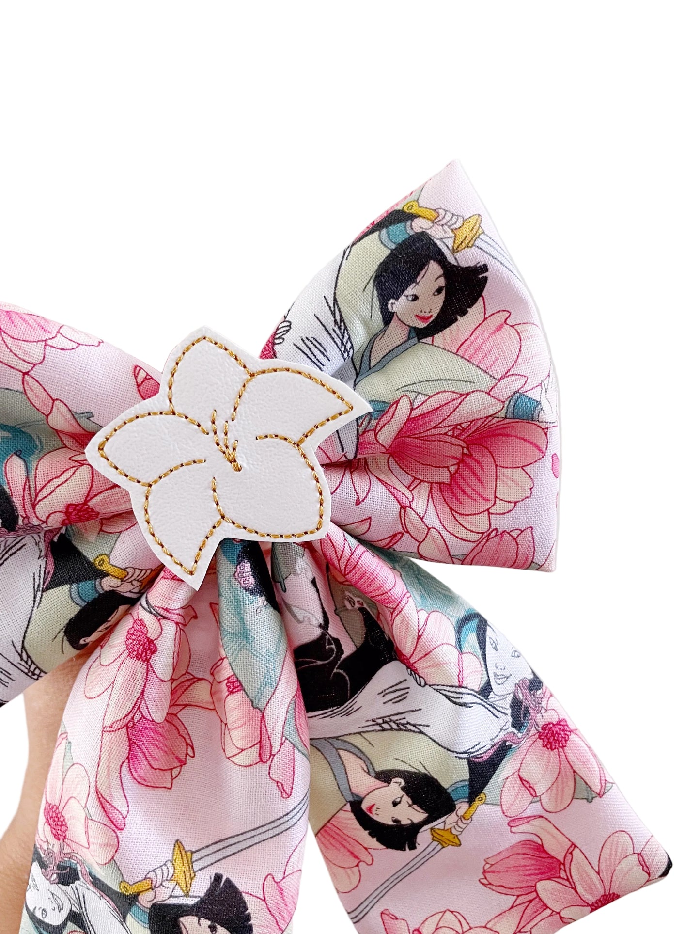 A close-up of a fabric hair bow featuring a pink and white floral print with cartoon characters, secured with a white flower-shaped hair clip.