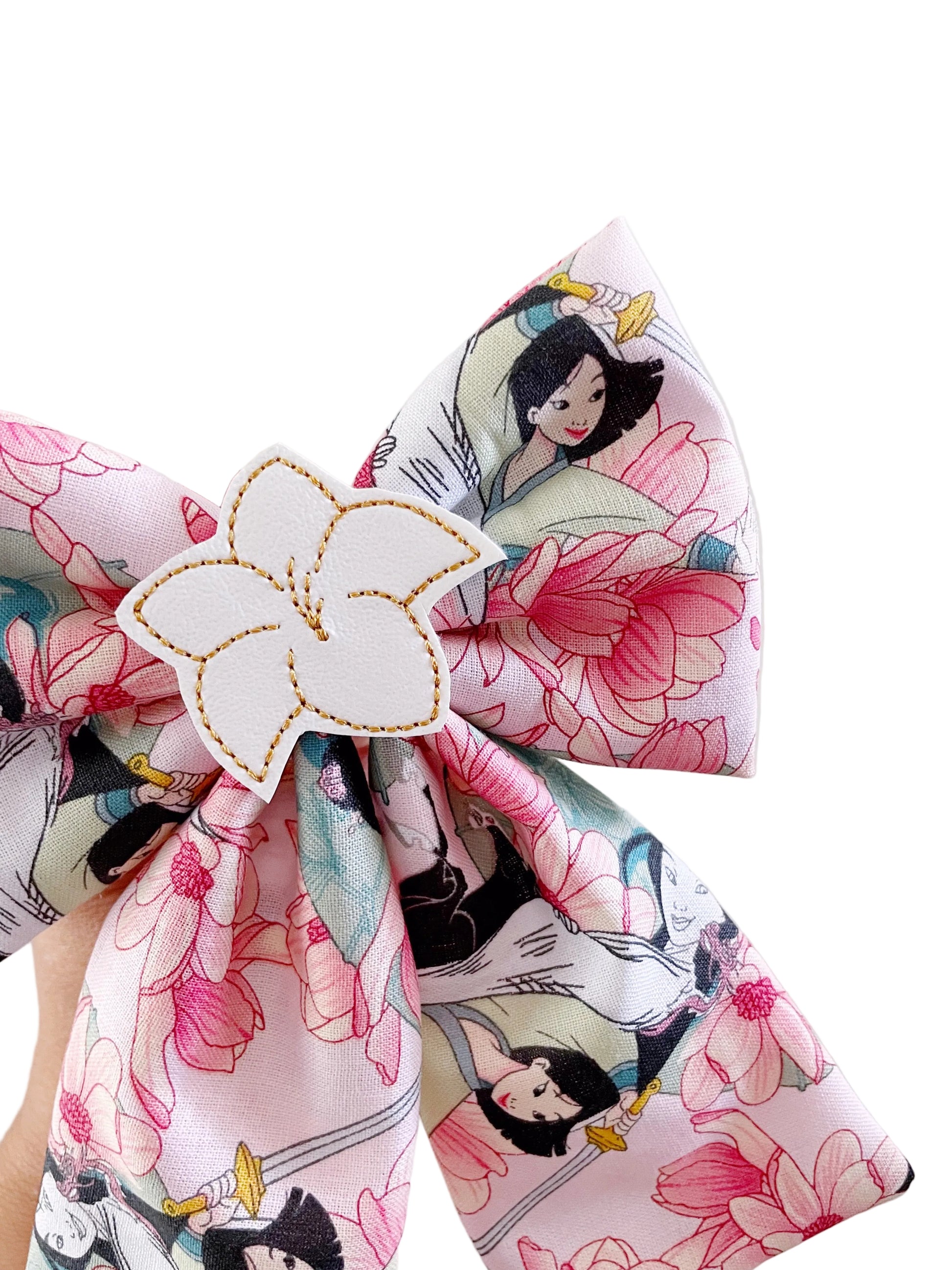A close-up of a fabric hair bow featuring a pink and white floral print with cartoon characters, secured with a white flower-shaped hair clip.